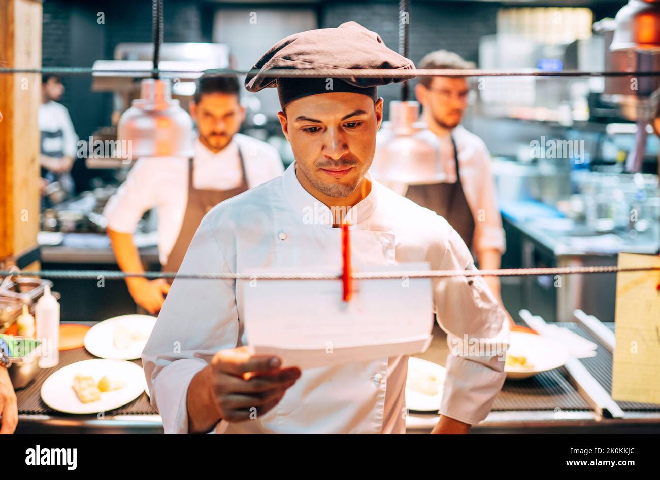 Chef in hat reading order on paper hanging on string while working in ...