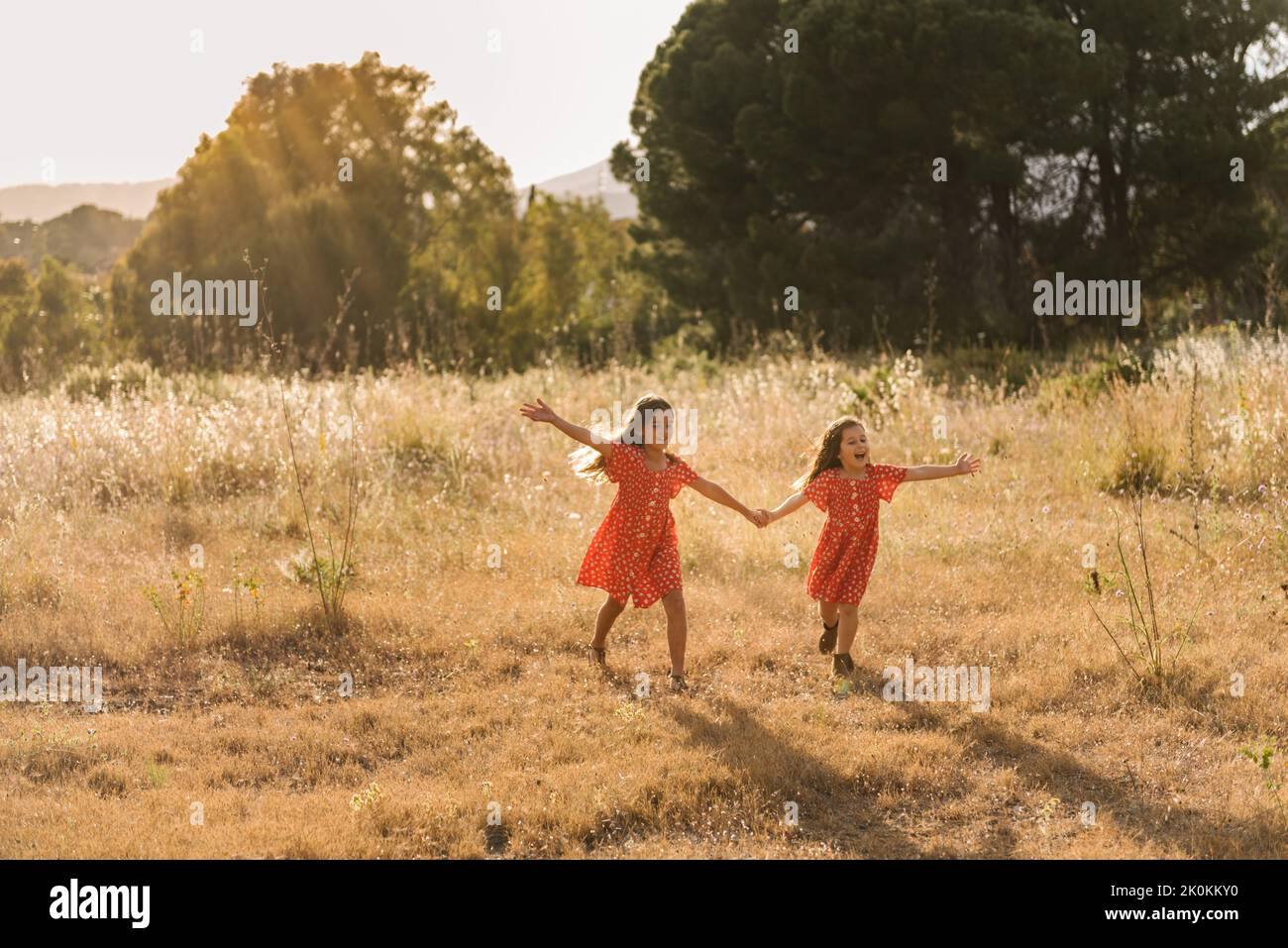Adorable happy sisters in red dresses holding hands and running on ...