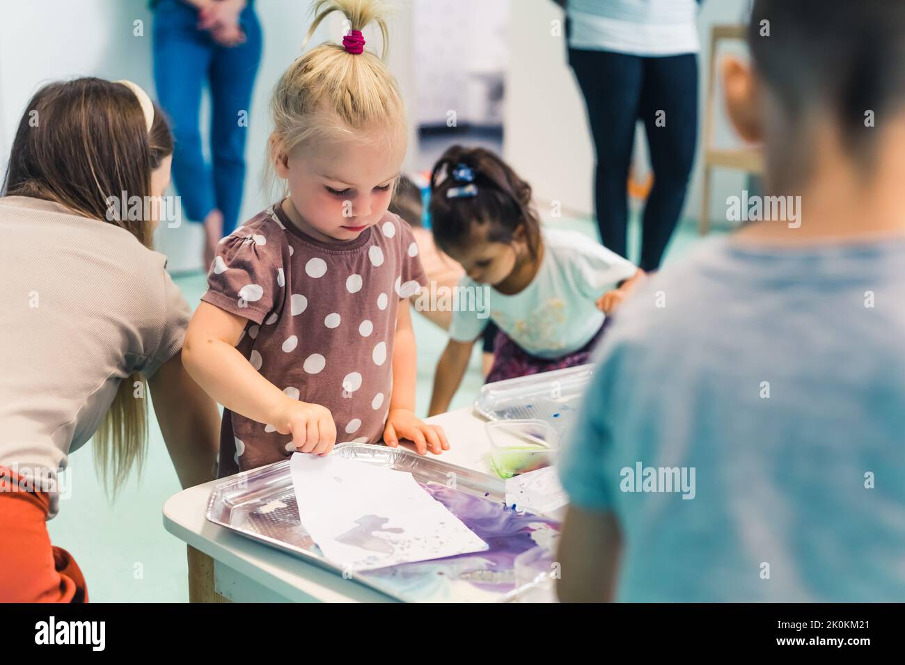 Little caucasian cute girl with other children milk painting, adding