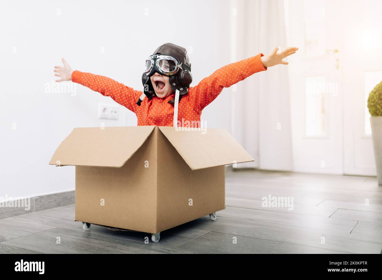 Little kid wearing goggles and aviator helmet while sitting in carton