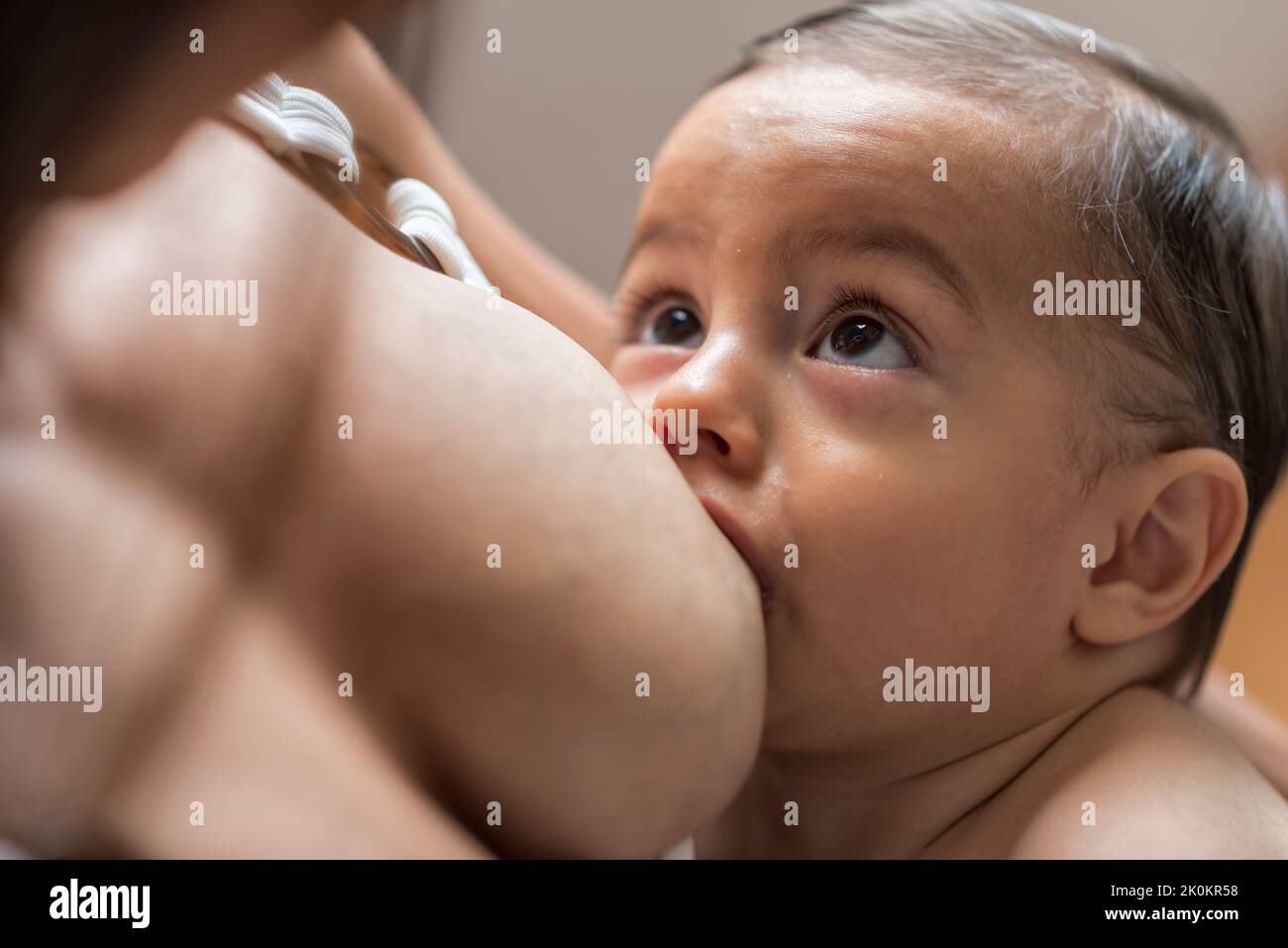 Mother breastfeeding cute infant in child room in daylight Stock Photo