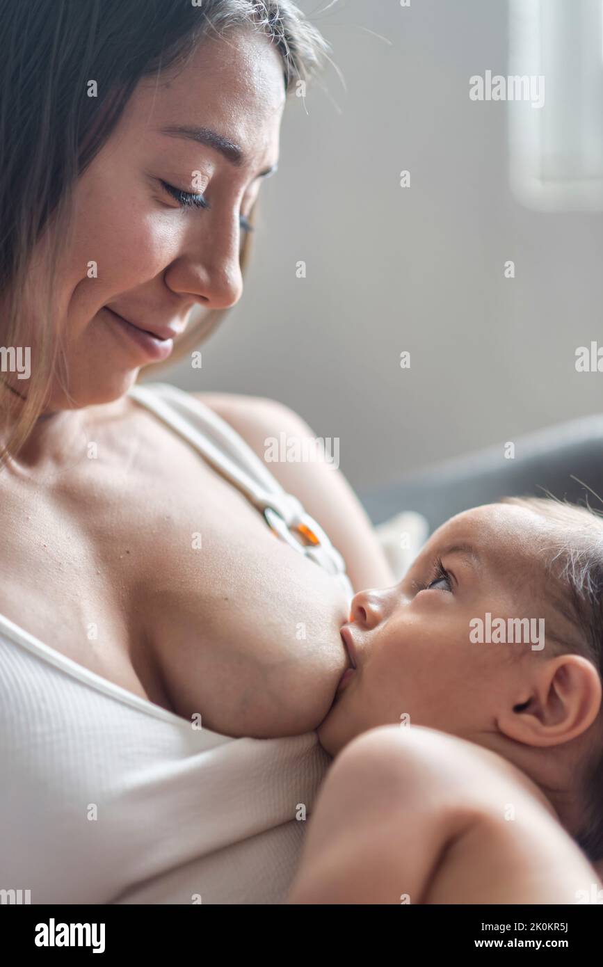 Mother breastfeeding cute infant in child room in daylight Stock Photo