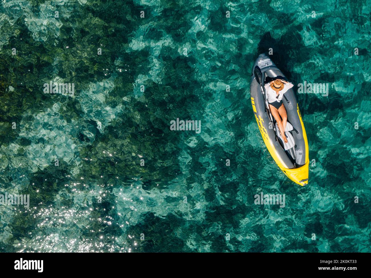 A lonely female in a straw hat relaxing lying in floating inflatable kayak on the turquoise