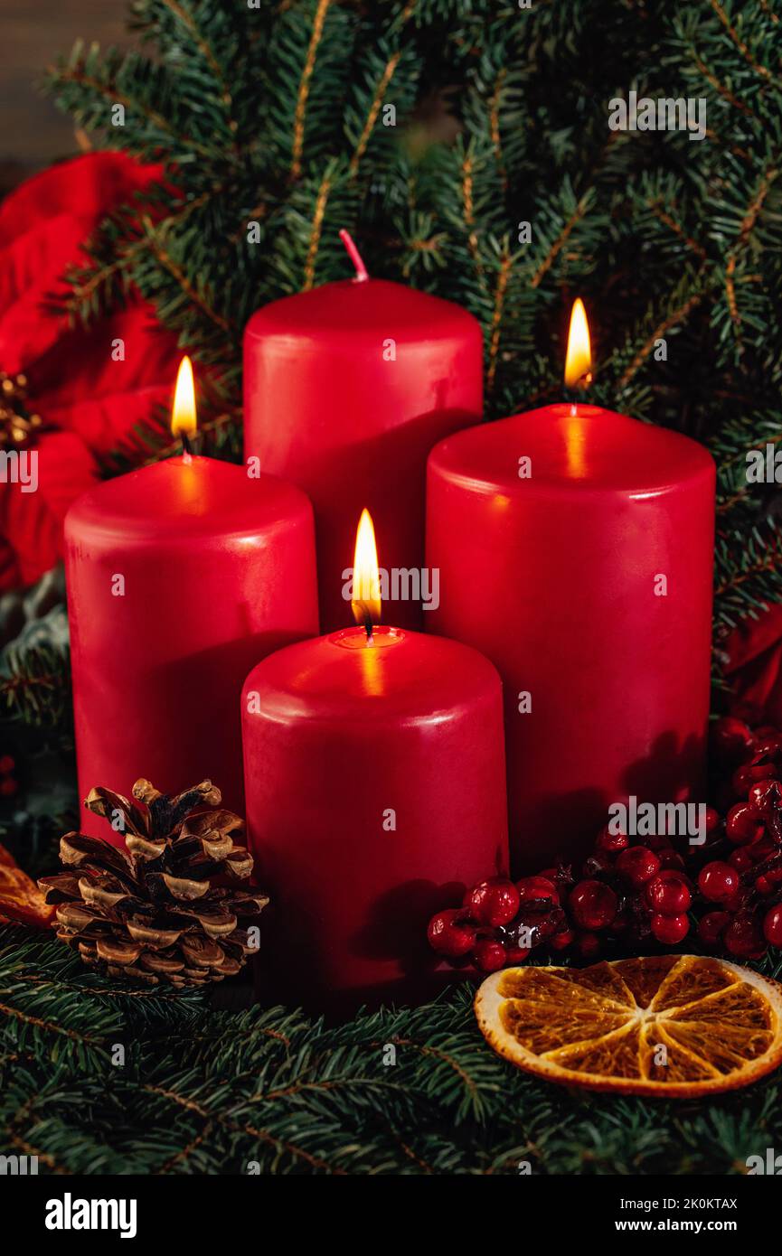 Three burning Red advent candles in advent wreath decoration on wooden