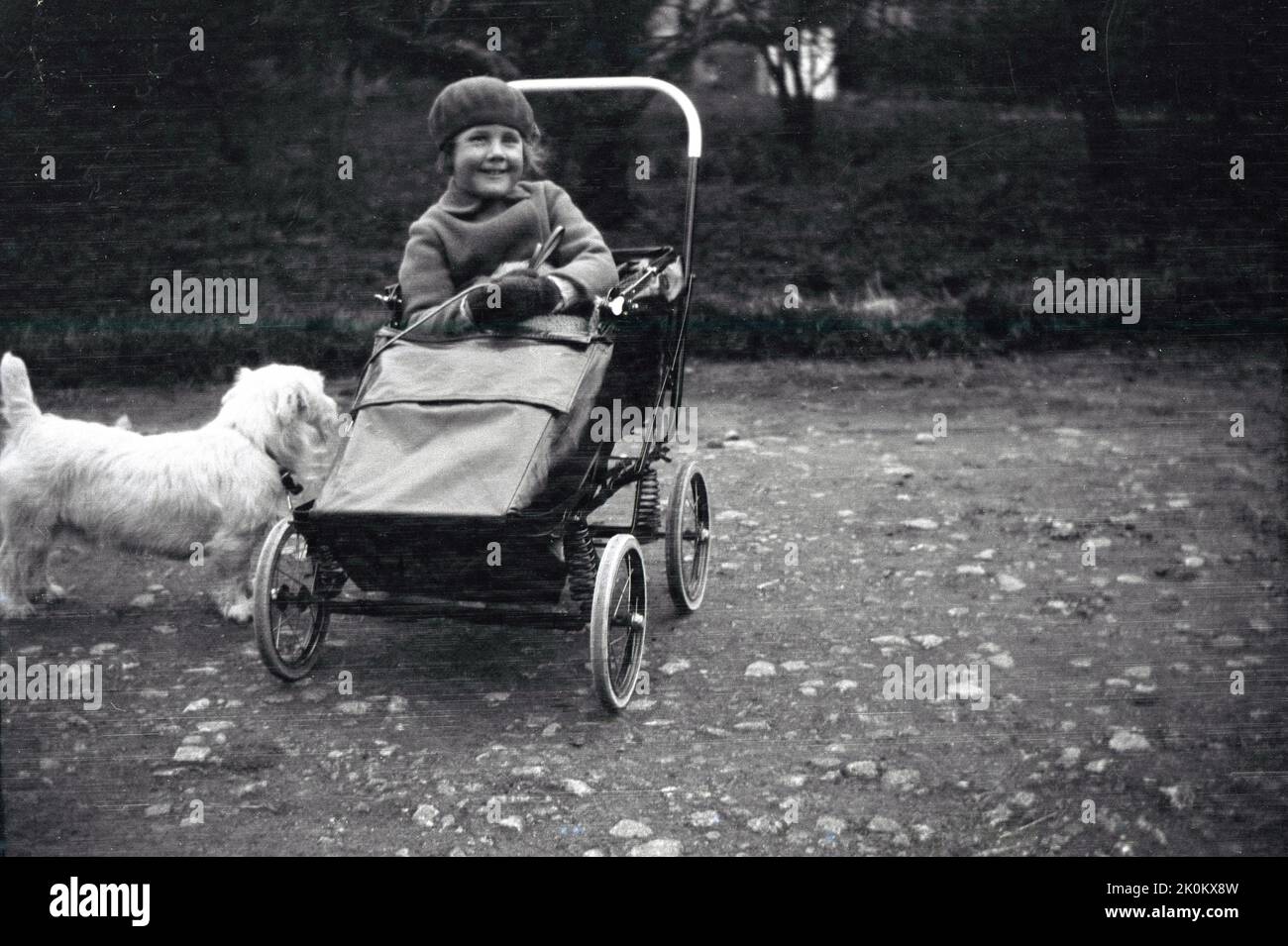 1932, historical, outside on rough ground, a young girl sitting in a pushchair of the era, with coiled sprung suspension, holding onto the lead of her pet scottie dog, England, UK. Stock Photo