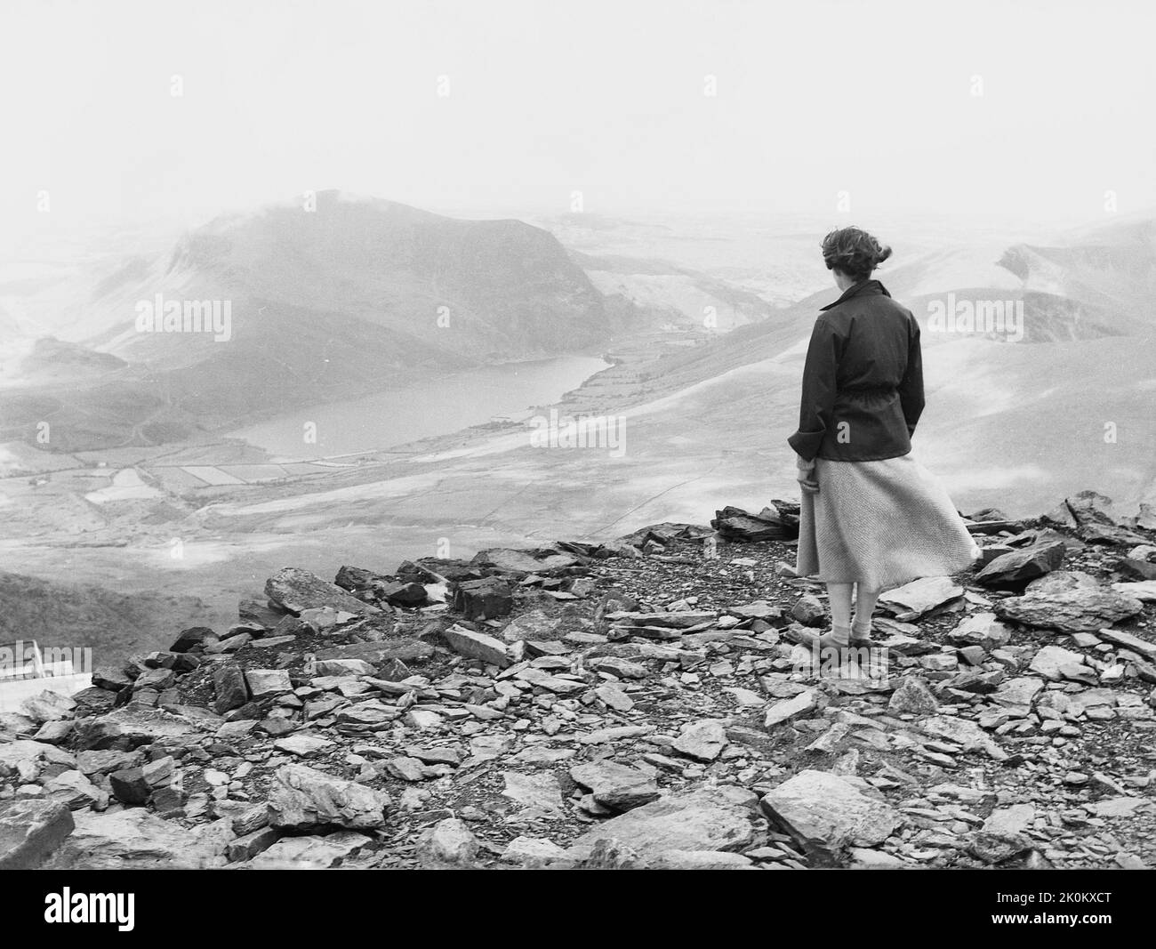 1956, historical, a lady, wearing a jacket and woolen skirt, standing on rocks and slates on a high level ridge in the Snowdonia mountains, Wales, UK, looking over the valley and landscape below. Stock Photo