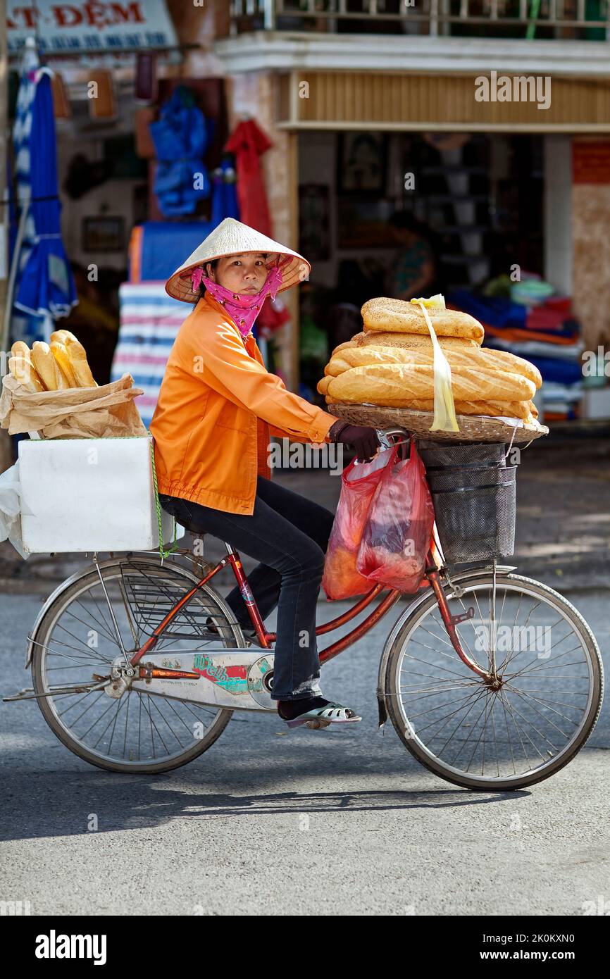 Vietnamese vendor wearing bamboo hat selling French bread from bicycle in the street, Hai Phong, Vietnam Stock Photo