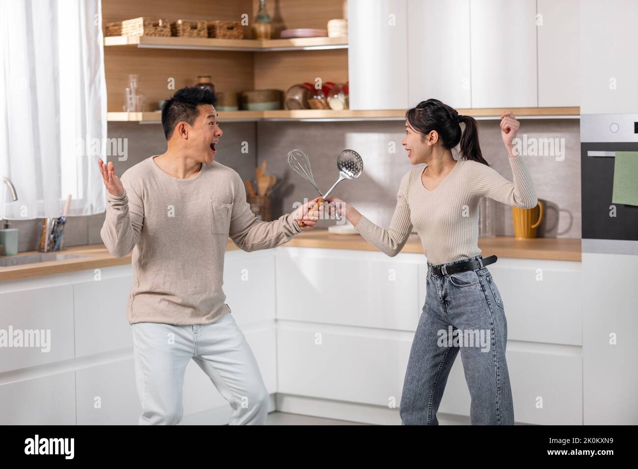 Positive chinese couple having fun while cooking at kitchen Stock Photo