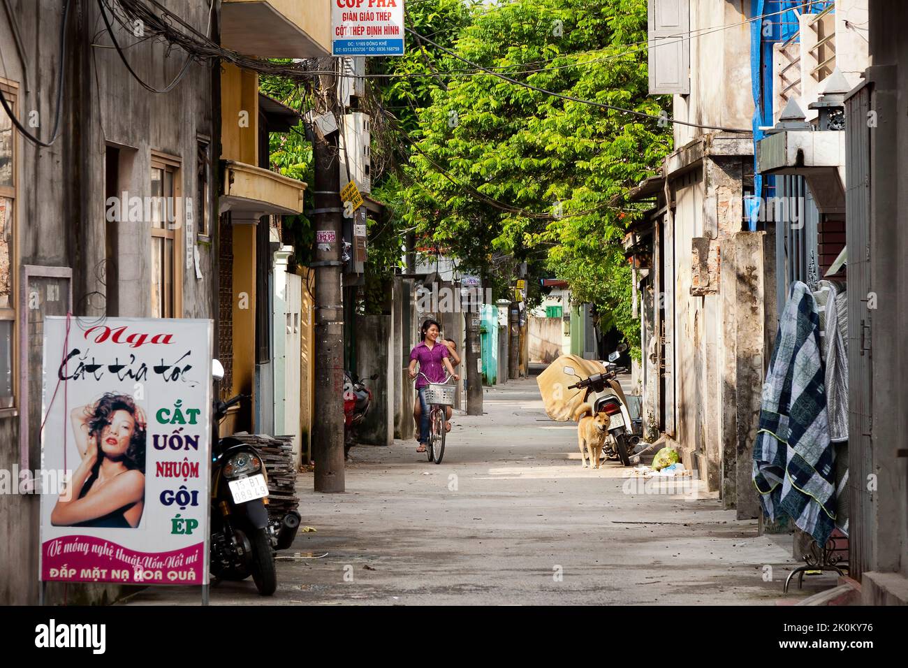 Vietnamese girls riding bicycle through narrow street, Hai Phong, Vietnam Stock Photo