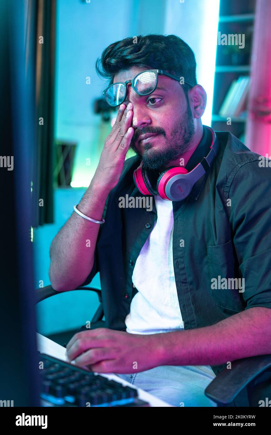 vertical shot of exhausted or tired gamer rubbing his eyes while playing video game during late night - concept of gaming addiction and health care. Stock Photo