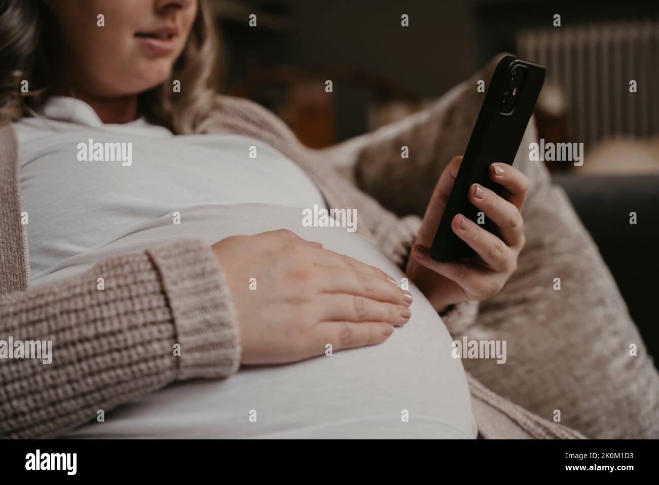Pregnant woman siting on her sofa using her cellphone Stock Photo