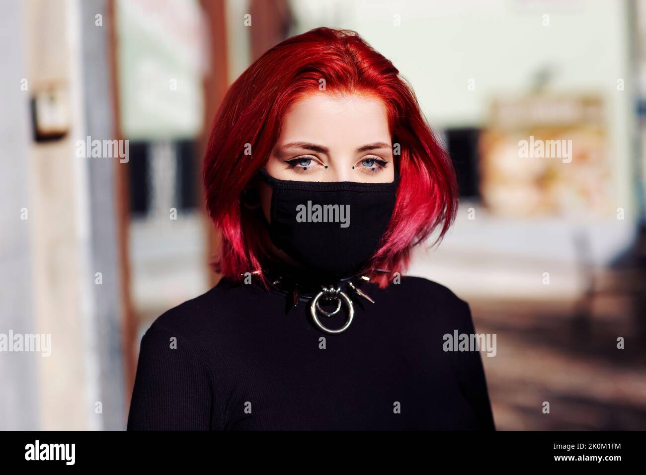 close up young adult woman outside with face mask blue eyes with punk spike choker redhead Stock Photo