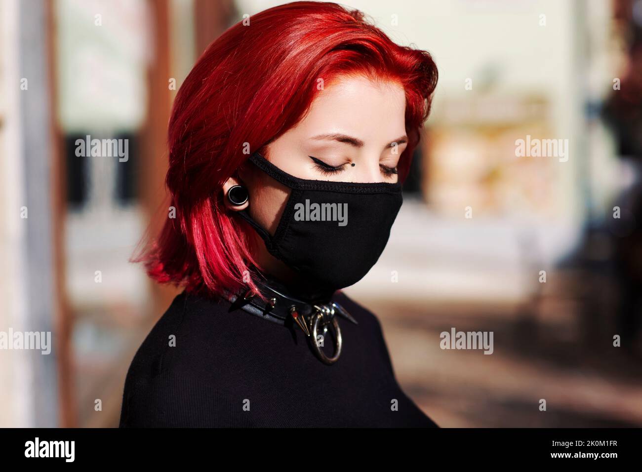 close up young adult woman outside with face mask blue eyes with punk spike choker redhead Stock Photo