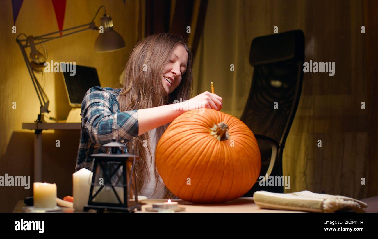 Preparing pumpkin for Halloween. Woman sitting and marking pumpkin with pencil before carving halloween Jack O Lantern at home for her family. Stock Photo