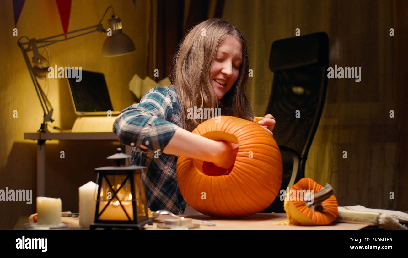 Preparing pumpkin for Halloween. Woman sitting and pulling out face details of carved halloween Jack O Lantern pumpkin at home for her family. Stock Photo