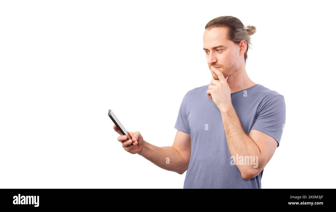 Man looks thoughtfully at his smartphone and rubs his chin. Concept of internet communication, fraud, discretion Stock Photo