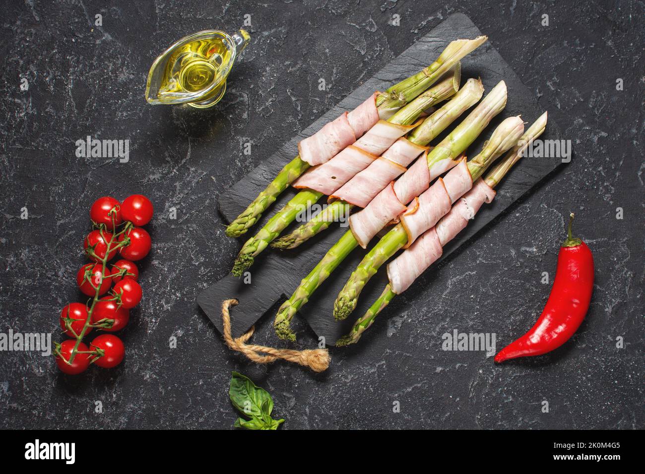 Fresh green asparagus wrapped in bacon on a black stone table. Top view Stock Photo