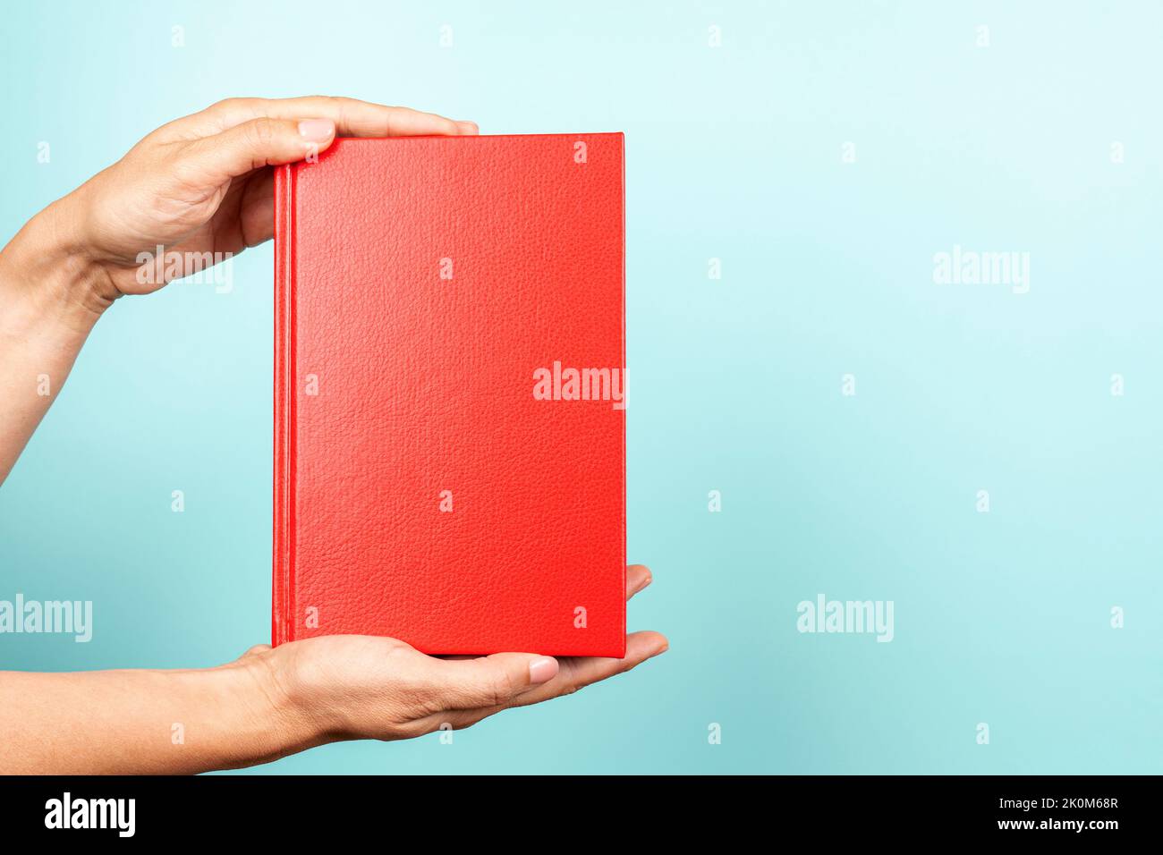 Woman hands holding book with blank red cover over light blue background. Education, back to school, self-learning, book swap, sharing, bookcrossing Stock Photo