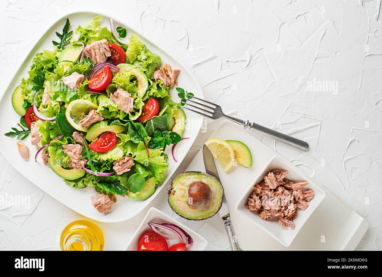 Fresh green leafy salad with tuna avocado and tomato on white table background. Concept for a tasty and healthy meal Stock Photo