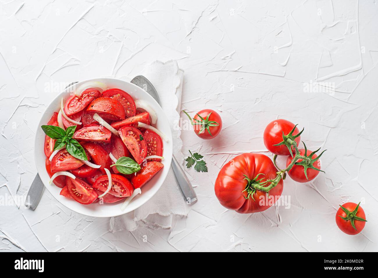 Fresh tomato salad with onion and basil on white table background. Concept for a tasty and healthy meal Stock Photo