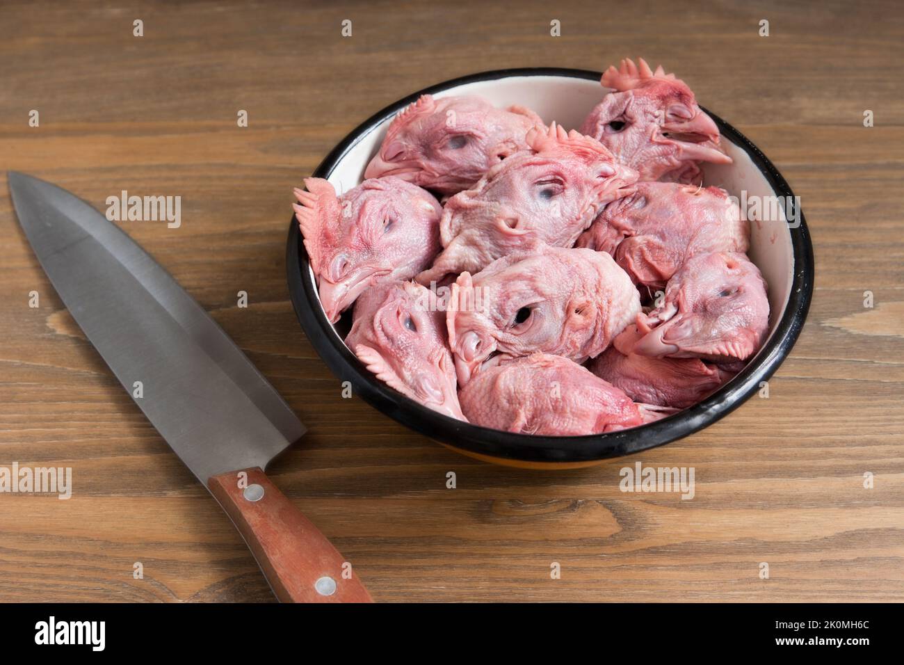Raw chicken heads in the metal dish and a big knife Stock Photo