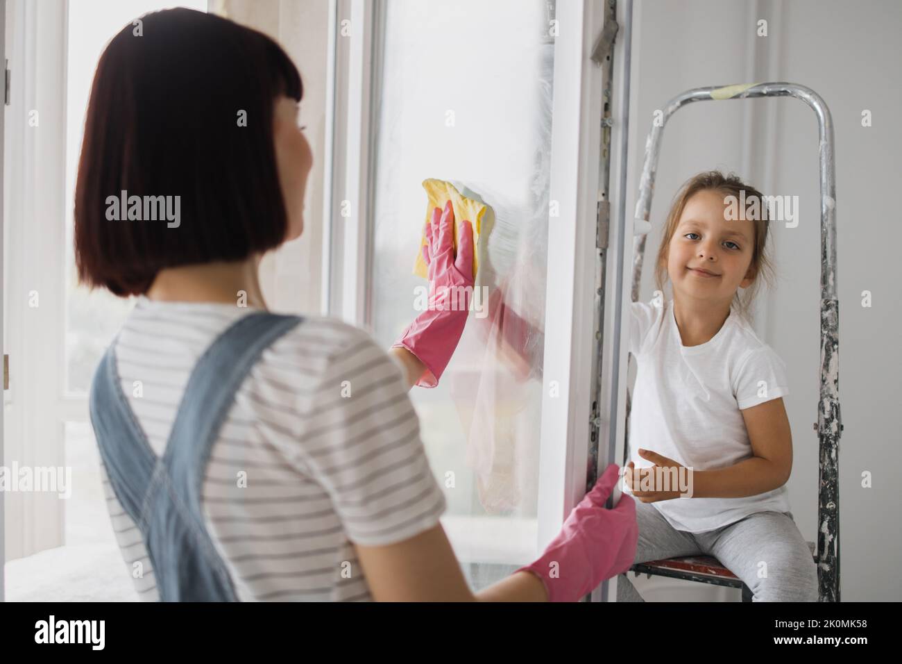 Beautiful caucasian mother and daughter cleaning window together in ...