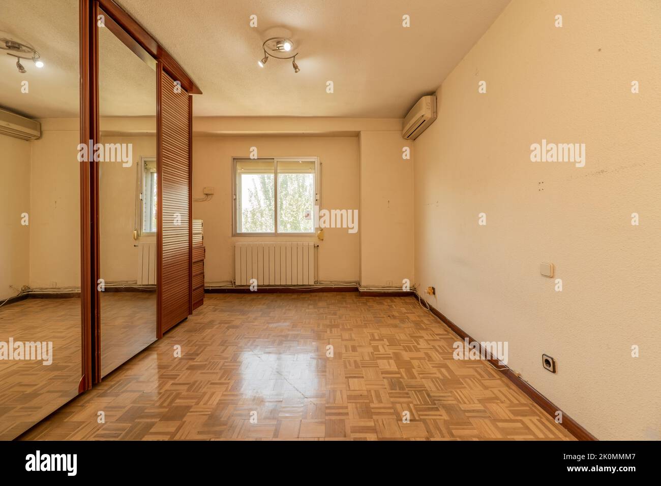empty room with gleaming oak parquet flooring, wall mounted air conditioner unit and three sliding mirror and venetian door wardrobe Stock Photo