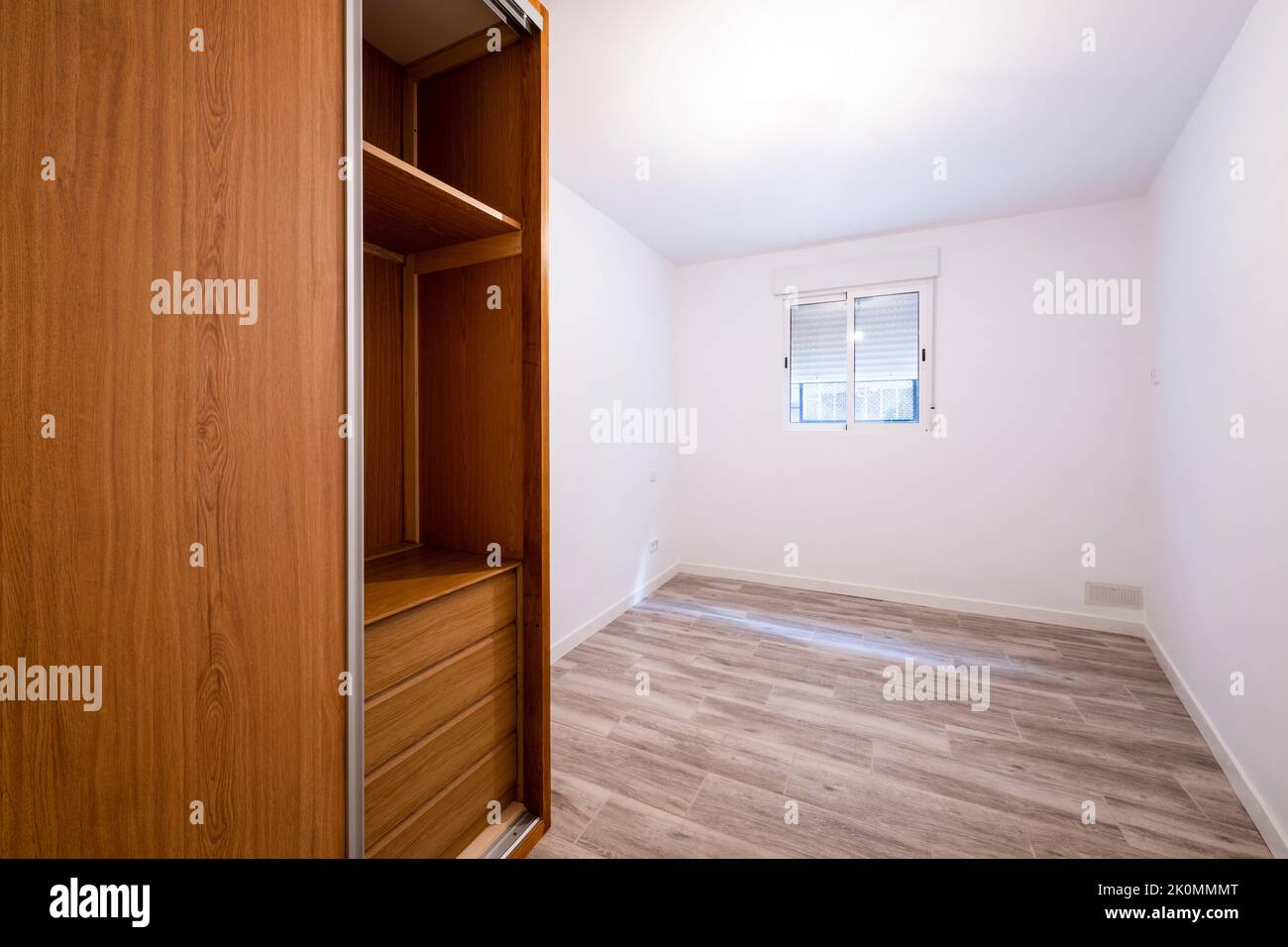 Renovated room with built-in wardrobe with sliding doors in cherry wood color, interior chest of drawers, white aluminum window and aluminum radiator Stock Photo