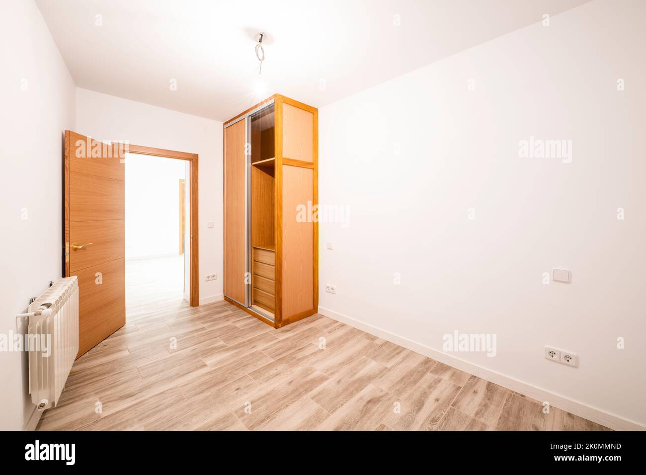 Renovated room with built-in wardrobe with sliding doors in cherry wood color, interior chest of drawers, matching front door and aluminum radiator on Stock Photo