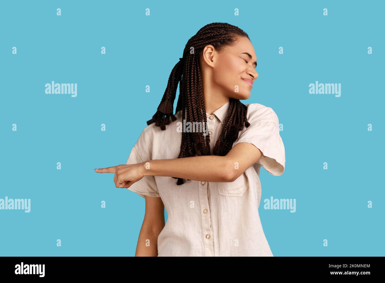 Get out. Irritated upset woman with black dreadlocks pointing away, quarreling and scolding, showing exit with angry grimace, feeling betrayed. Indoor studio shot isolated on blue background. Stock Photo