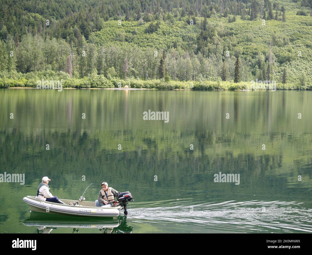 Alaska USA August 11 2008; Couple fishing from small inflatable on calm water surrounded by wilderness reflected deep into water. Stock Photo