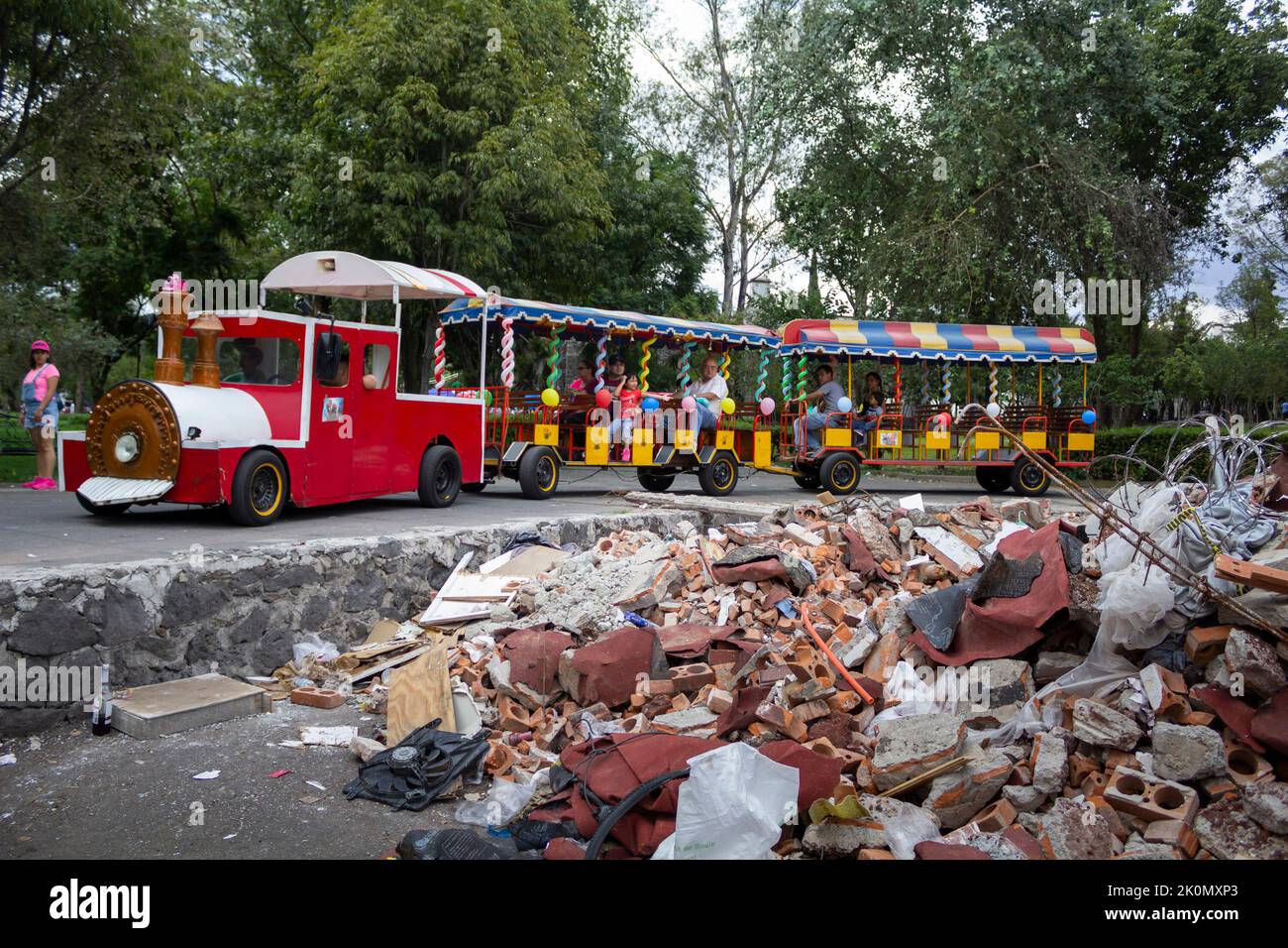 People riding a park train looking at building debris. In 2017, an 8.1 ...