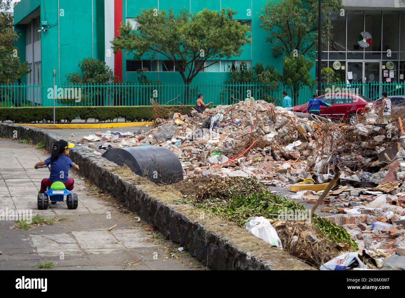 A kid riding a tricycle and looking at a building collapsed building ...
