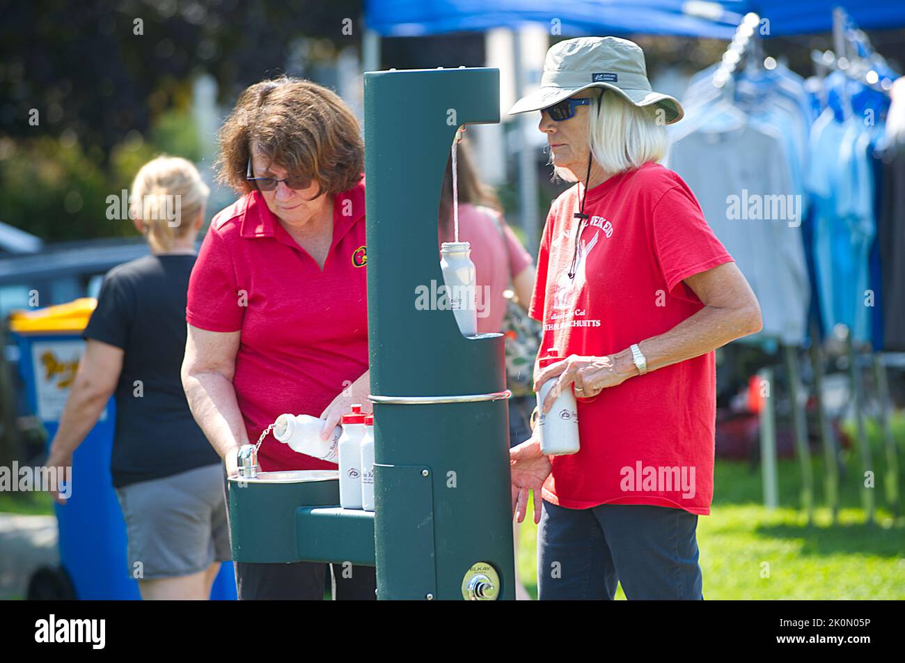 Two women using a water bottle refilling station at the Eastham Windmill Weekeng fair on Cape Cod, USA Stock Photo
