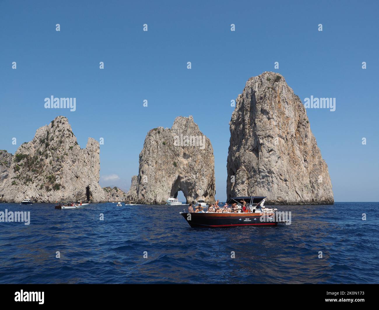 Tourist boats at the iconic Faraglioni rocks while making a tour around the island. Capri, Campania, Italy Stock Photo
