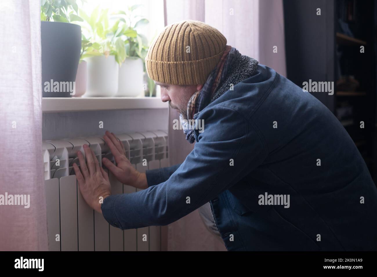 Man wearing warm clothing feeling cold checking central heating battery. Energy crisis in Europe Stock Photo