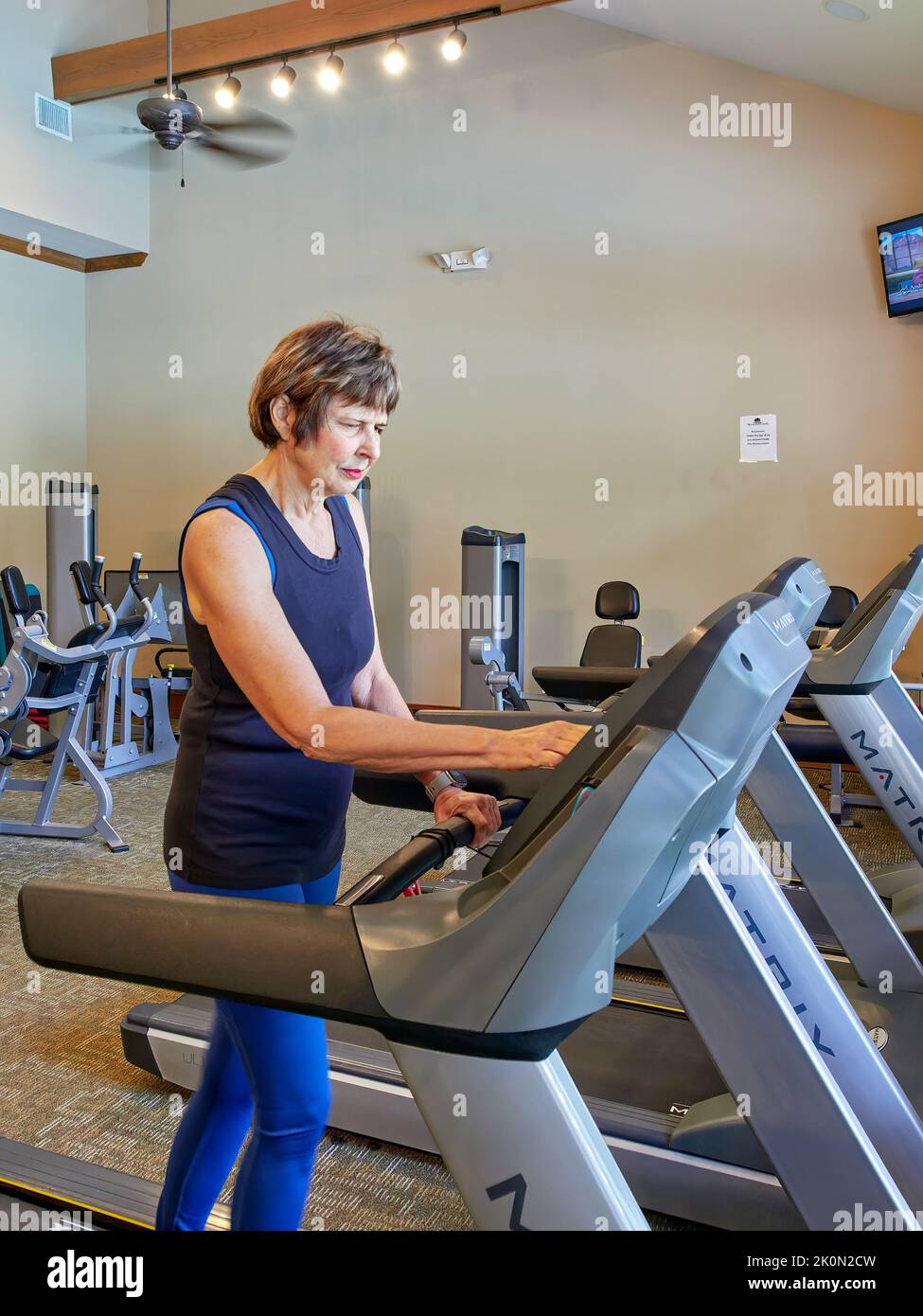 Middle aged mature or senior woman using or running on or using a treadmill in a gym. Stock Photo
