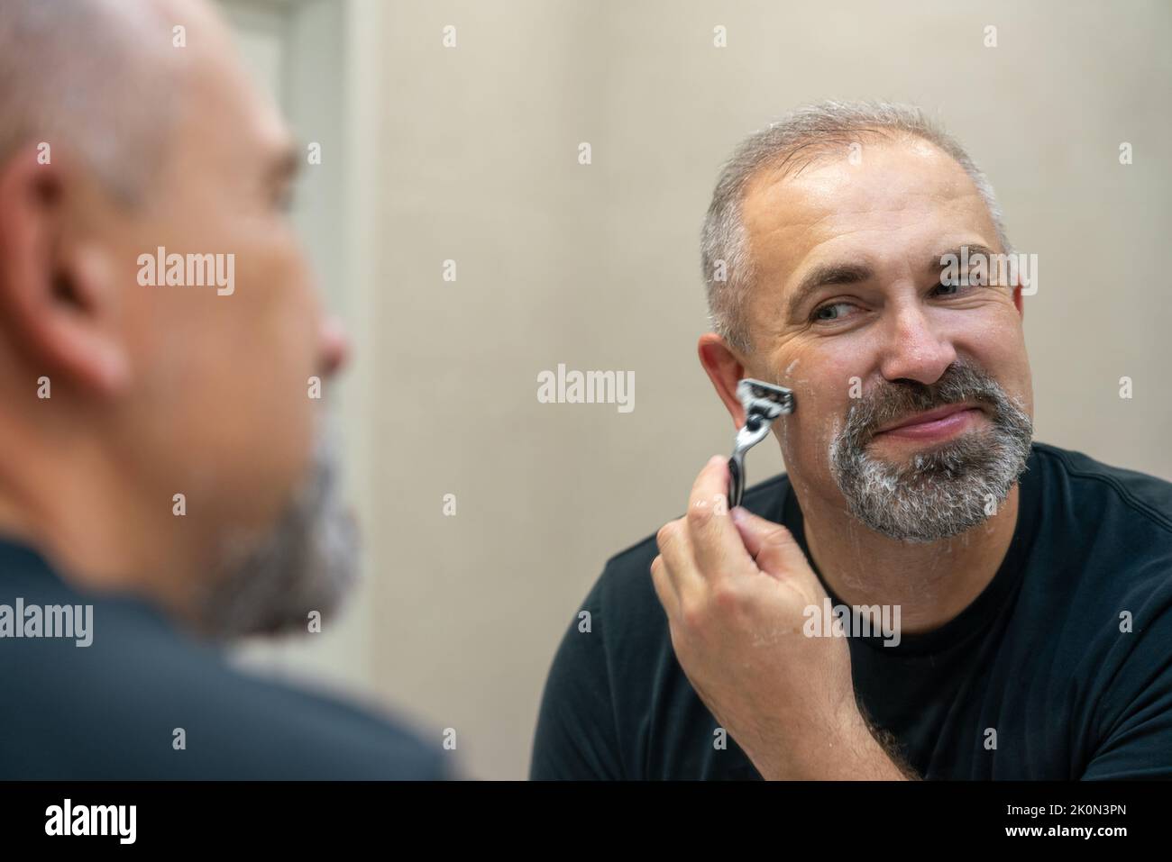 Middle-aged handsome man using razor in bathroom Stock Photo