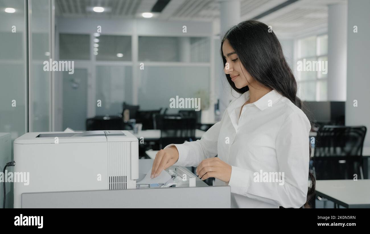 Arab hispanic businesswoman girl worker secretary makes copies on photocopier use office equipment print machine replicate papers sending fax printing Stock Photo
