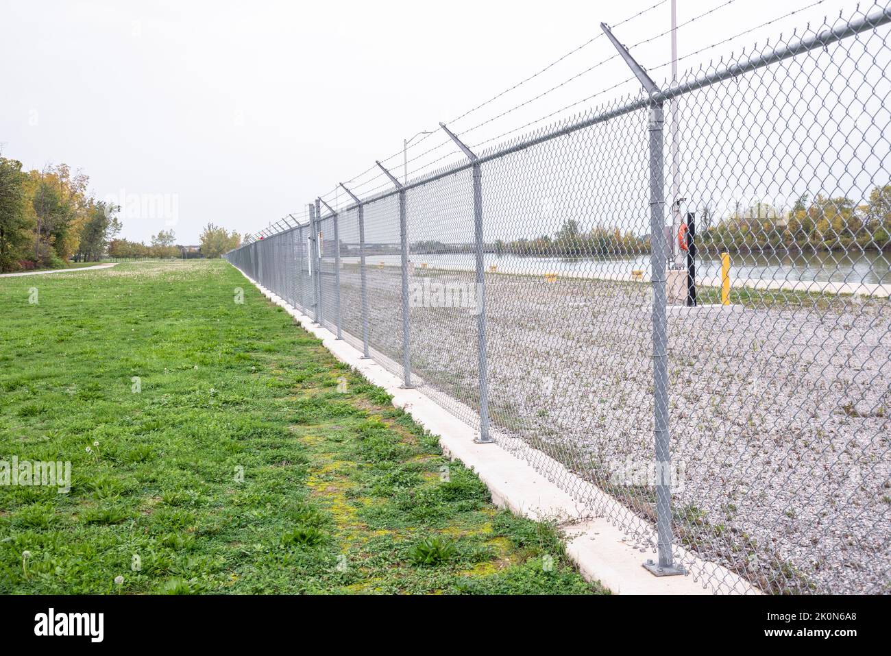 Chain-link fence along a navigable canal on a raining autumn day. Concept of security. Stock Photo