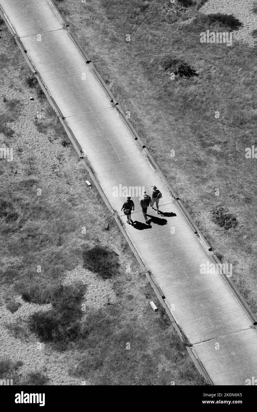 Monochrome image of three walkers on a road taken from above with shadows. Stock Photo