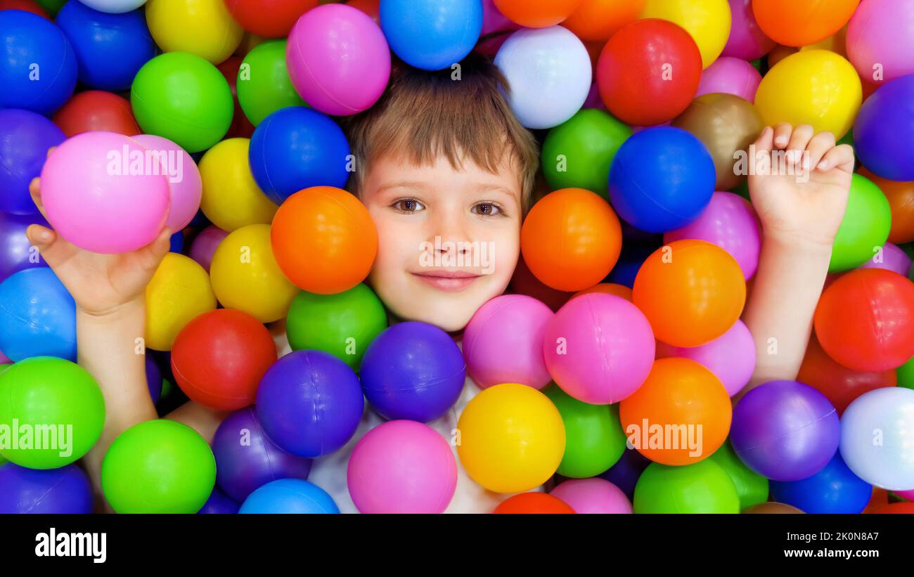 Smile kid lying colorful plastic balls pool. Colorful balls dry pool kindergarten playground child indoor play area. Playroom kids ball pit. Caucasian Stock Photo