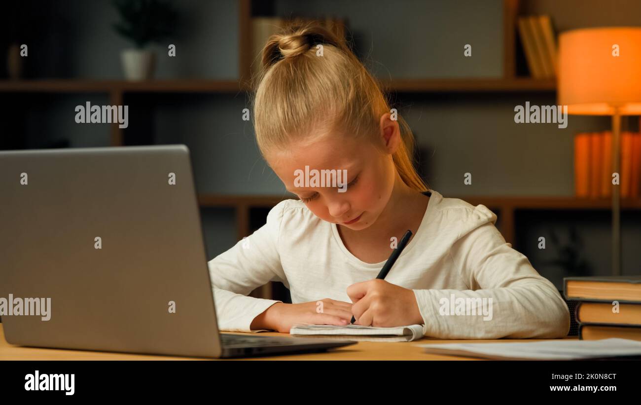 Smart pretty primary schoolgirl blonde little pupil seven years old kid studying in house room writing homework doing elementary math task imaging Stock Photo