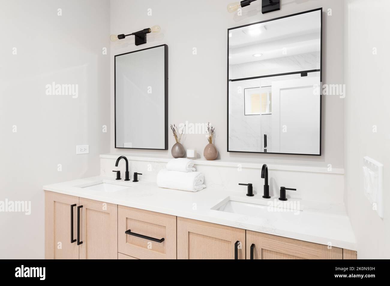 A modern bathroom with a wooden vanity black faucets, white