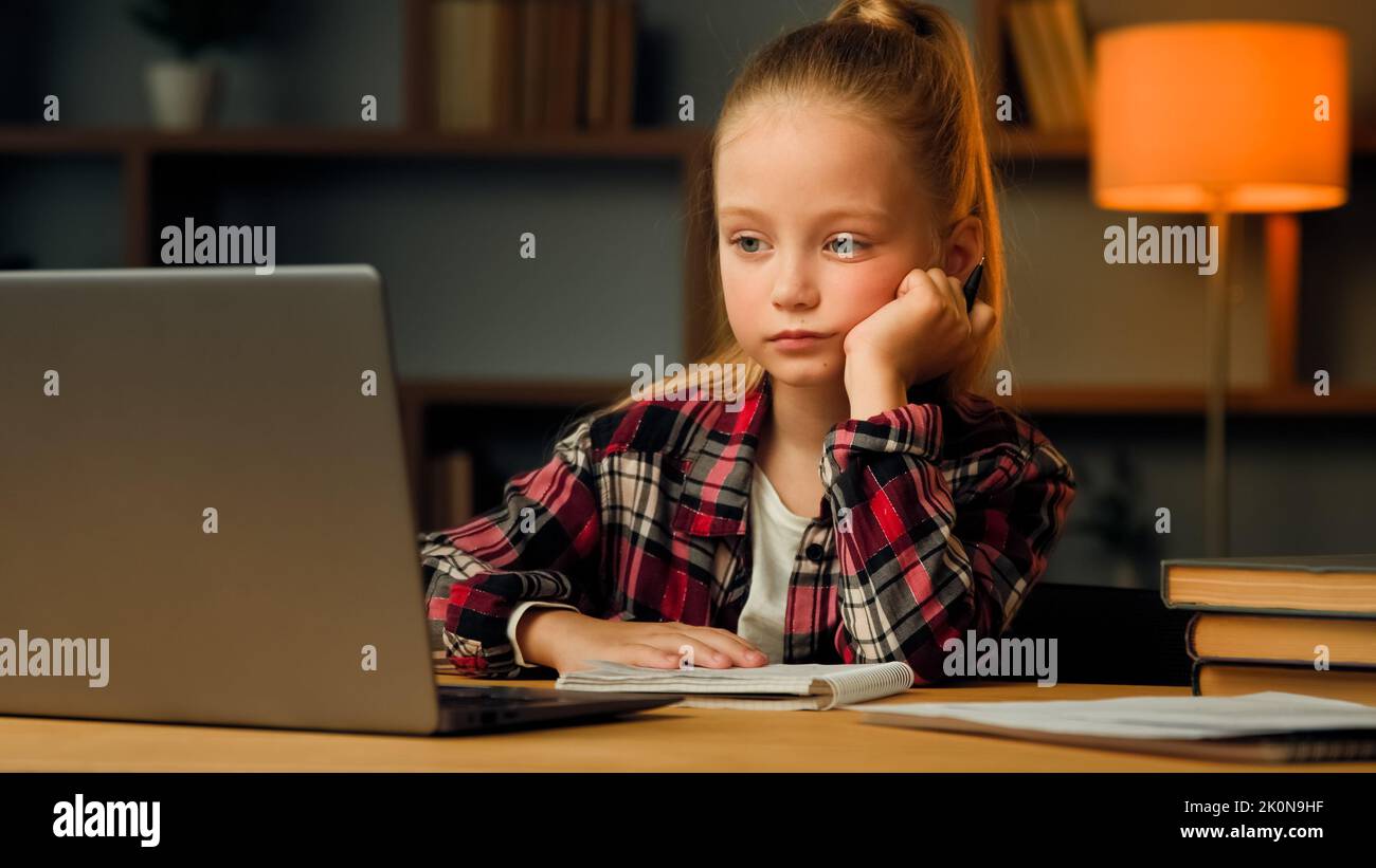 Weary sleepy caucasian young child blonde little lazy tired girl studying routine online elementary educational lesson on laptop napping at home Stock Photo