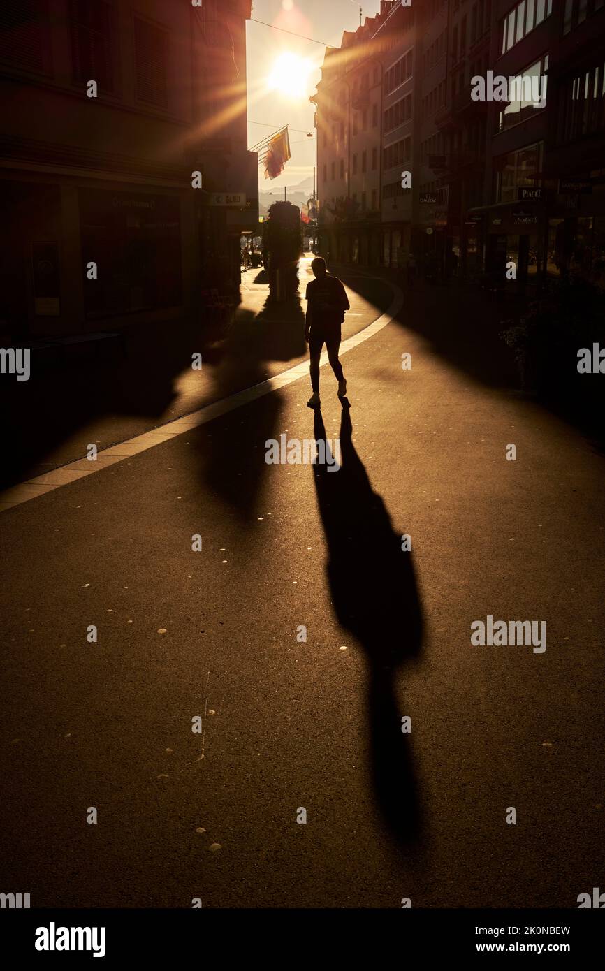 Anonymous pedestrian strolling on asphalt road at sundown Stock Photo