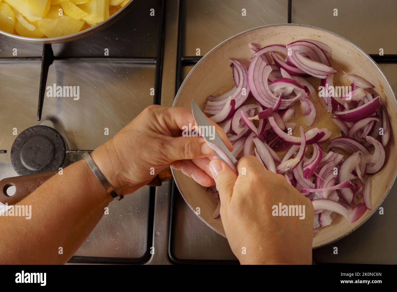 woman pouring shallot onion into a pan with boiling oil Stock Photo