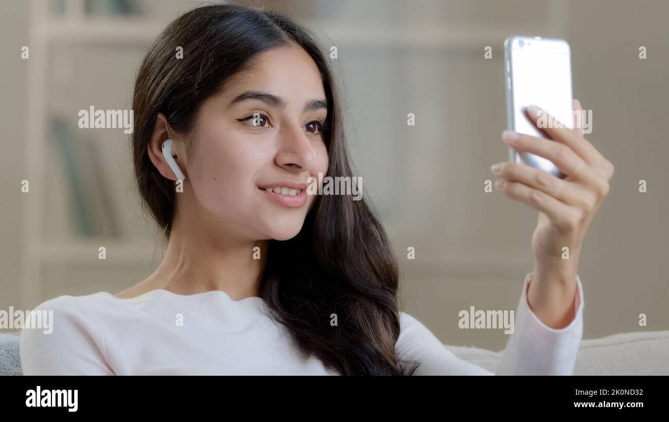 Female blogger arabic young girl beautiful pretty woman influencer in wireless earphones headphones talks at mobile camera takes self photo streaming Stock Photo