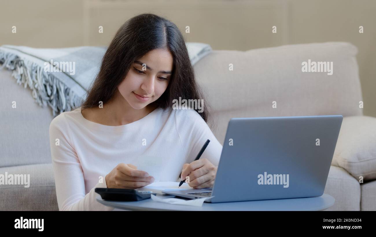 Young housewife arab middle eastern woman considers utilities uses calculator control domestic budget counts incomes outcomes bills writes notes Stock Photo