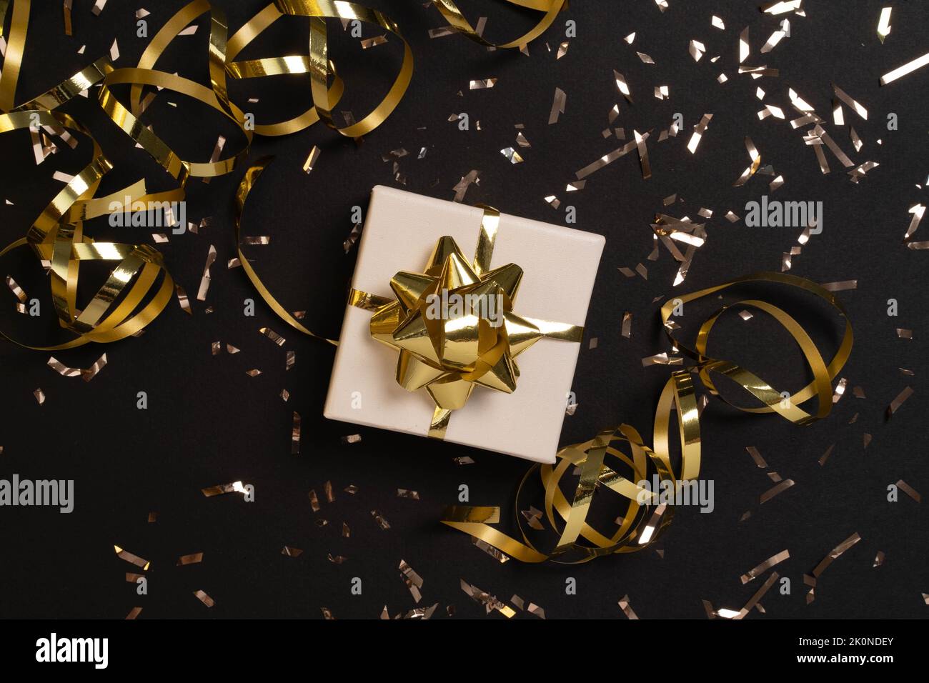 Gift or present box and gold confetti on black table top view. Flat lay composition for christmas, new year , birthday, mother day, black friday , sale, promotions, xmas, or wedding.  Stock Photo